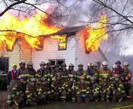 foto del cuerpo de bomberos y edificio ardiendo tras ellos